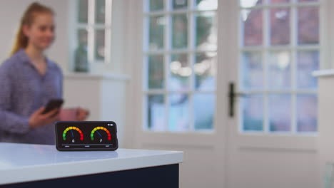 woman with drink and mobile phone walking past smart energy meter measuring electricity and gas use at home - shot in slow motion