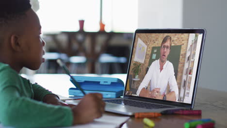 niño afroamericano haciendo la tarea mientras tiene una videollamada con un profesor masculino en una computadora portátil en casa