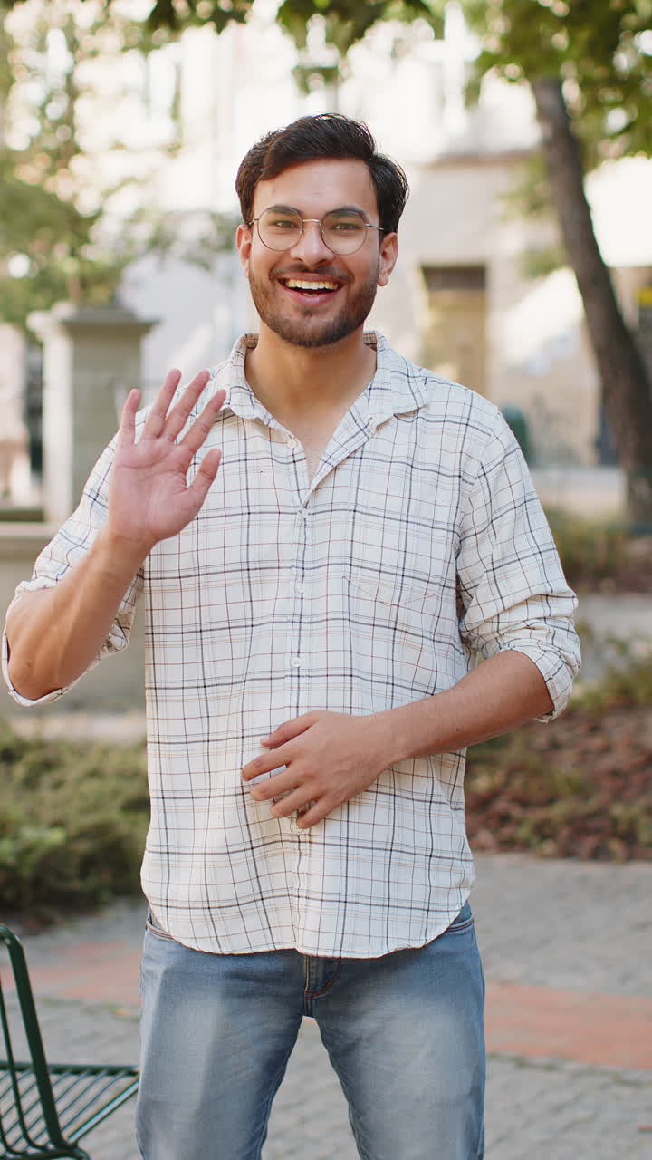 joven indio sonriendo amistosamente a la cámara hola agitando las manos gestando hola saludando en la calle