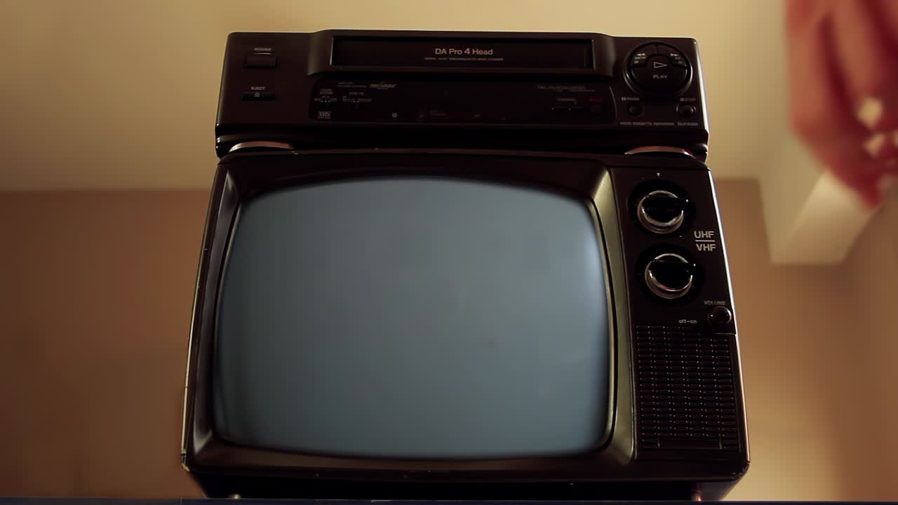Mano di un uomo che inserisce una VHS in un videoregistratore e una vecchia TV che si accende con schermo verde. Primo piano. Risoluzione 4K.