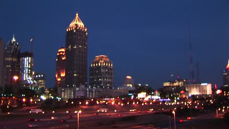 skyscrapers make up the background for an evening panning shot of traffic flowing along on an atlanta freeway