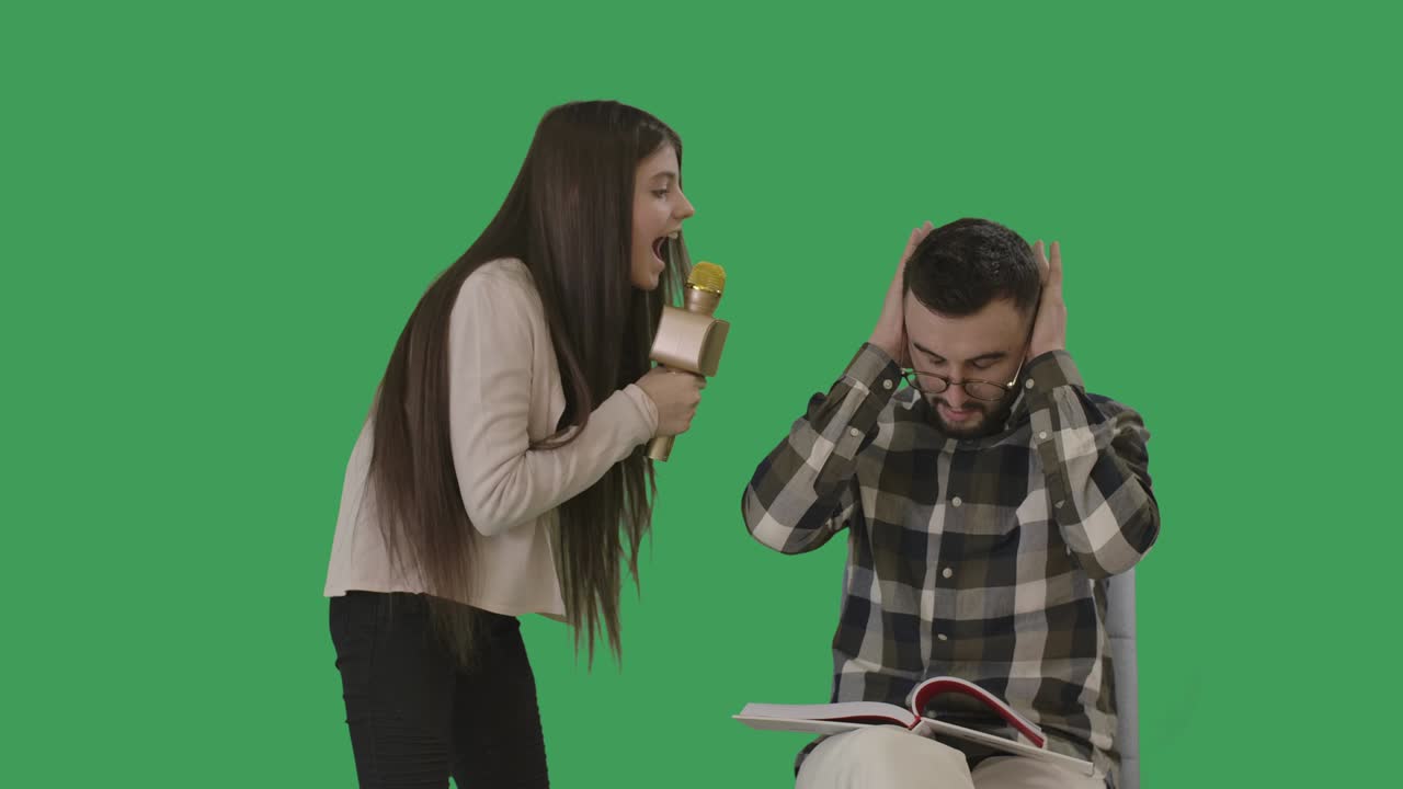 Joyful teenage girl singing out loud and distracting father from reading. Portrait of concentrated Caucasian man in eyeglasses bothered by daughter. Lifestyle. Chromakey. Cinema 4k ProRes HQ.
