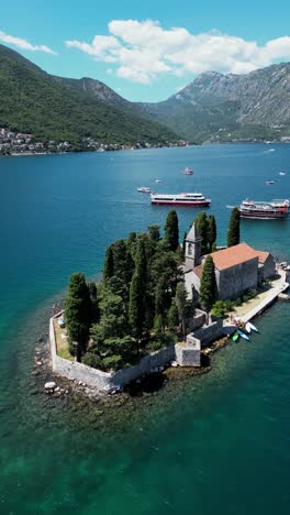 vertical aerial view of montenegro landscape with small island in the middle of kotor bay. drone circling around the islands. dozens of tourist boats in the bay. turquoise water color.