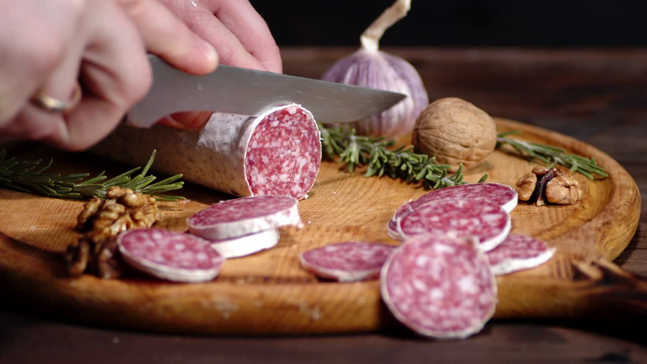 las manos de los hombres cortan salami con nueces y romero.