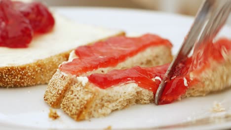 strawberry jam and buttered bread is cut into narrow slices on white dish, close up