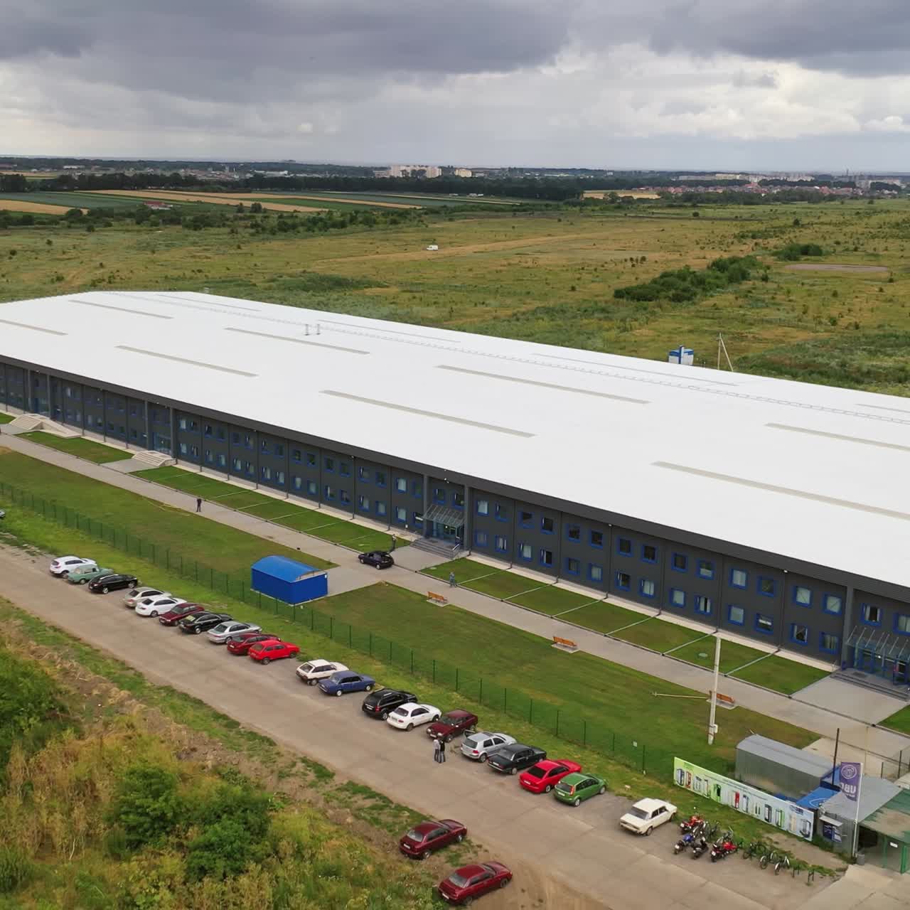 Aerial view of a large industrial building and parking lot surrounded by green fields