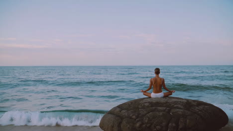 woman meditating on a rock by the ocean