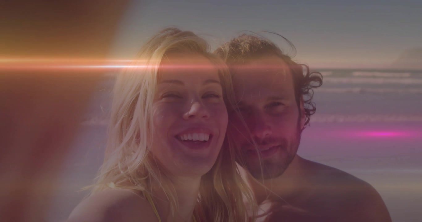 Coppia che tiene la fotocamera in avanti creando un bagliore dell'obiettivo che attraversa la spiaggia mentre sorridono per il viaggio