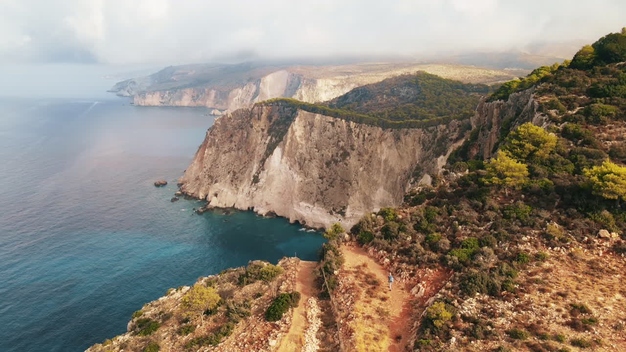 Aerial drone view of the Ionian Sea coast of Zakynthos, Greece. Tourist walking on the rocky cliff, vegetation, blue water. Sunset