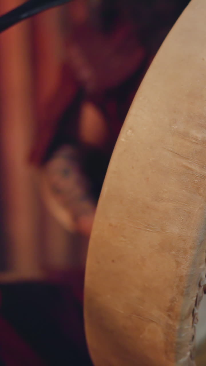 Musician taps shamanic drum with furry stick in ail cabin closeup. Siberian man conducts ancient mystical ritual. Folk music and performance