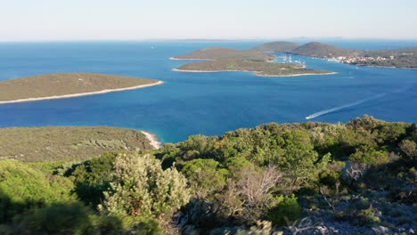 drone flying over the lush trees in the island of losinj overlooking boats cruising and leaving wake on the deep blue adriatic sea in croatia at summer - high angle shot