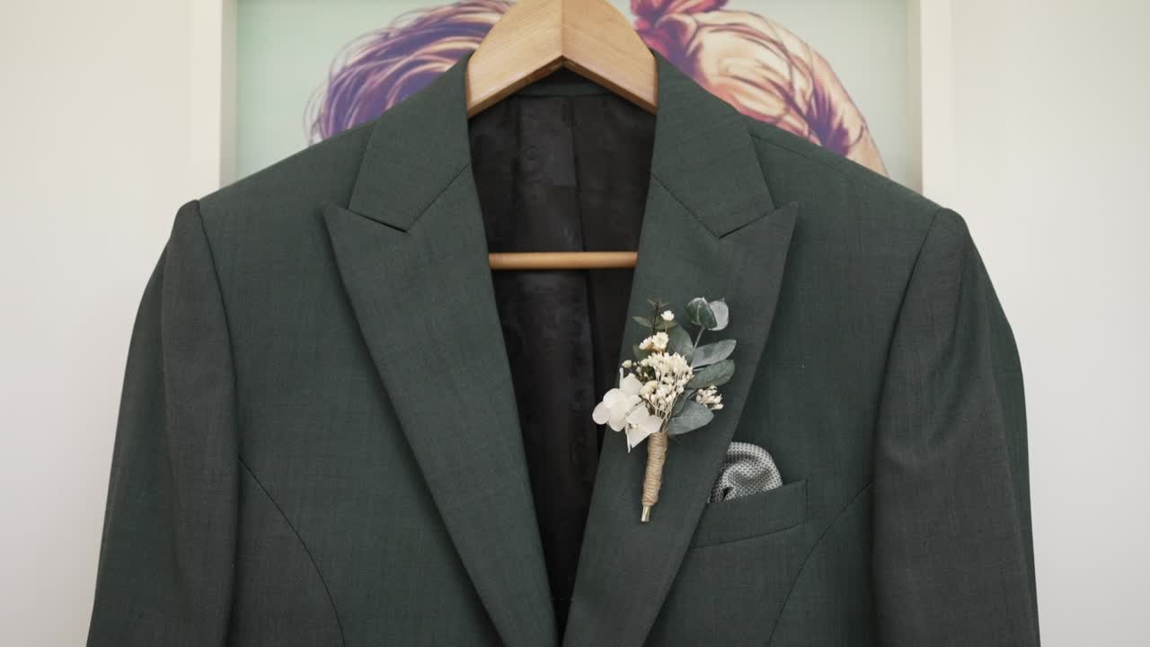 Groom’s suit with a boutonnière hanging on a wooden hanger, prepared for the wedding