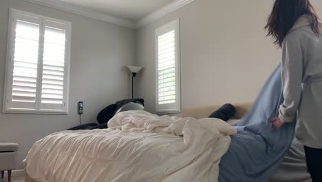 woman getting ready for a brand new start to a day. she stretches, gets up and out of bed, and fixes her bed coverings. white simple room with natural sunlight shining through window blinds.