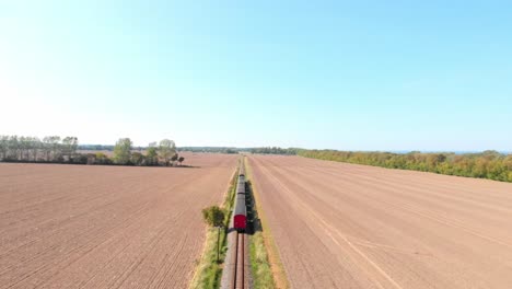 aerial: steam narrow gauge railway in the countryside passing by sown fields, flying above the train