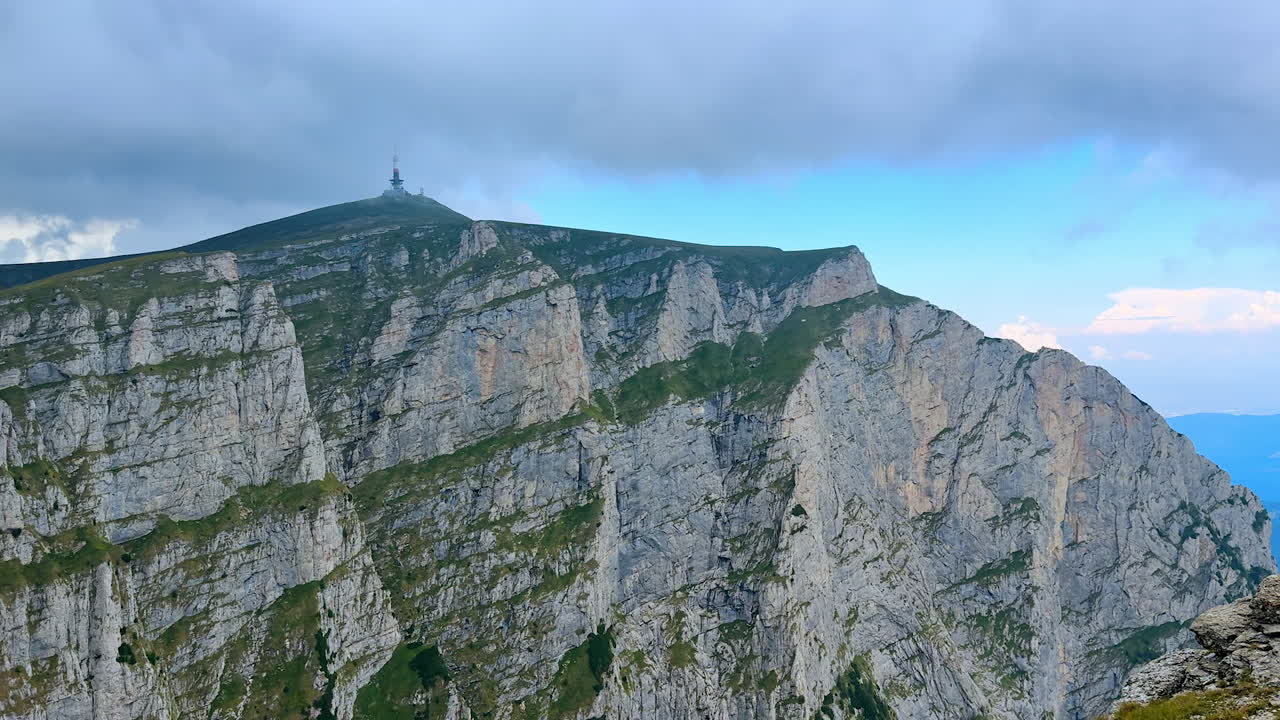 Radio tower half-hidden by the clouds on the huge rock. Stunning steep Bucegi mountains in Romania