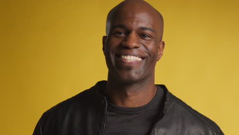 head and shoulders studio portrait of smiling and laughing mature man against yellow background 1