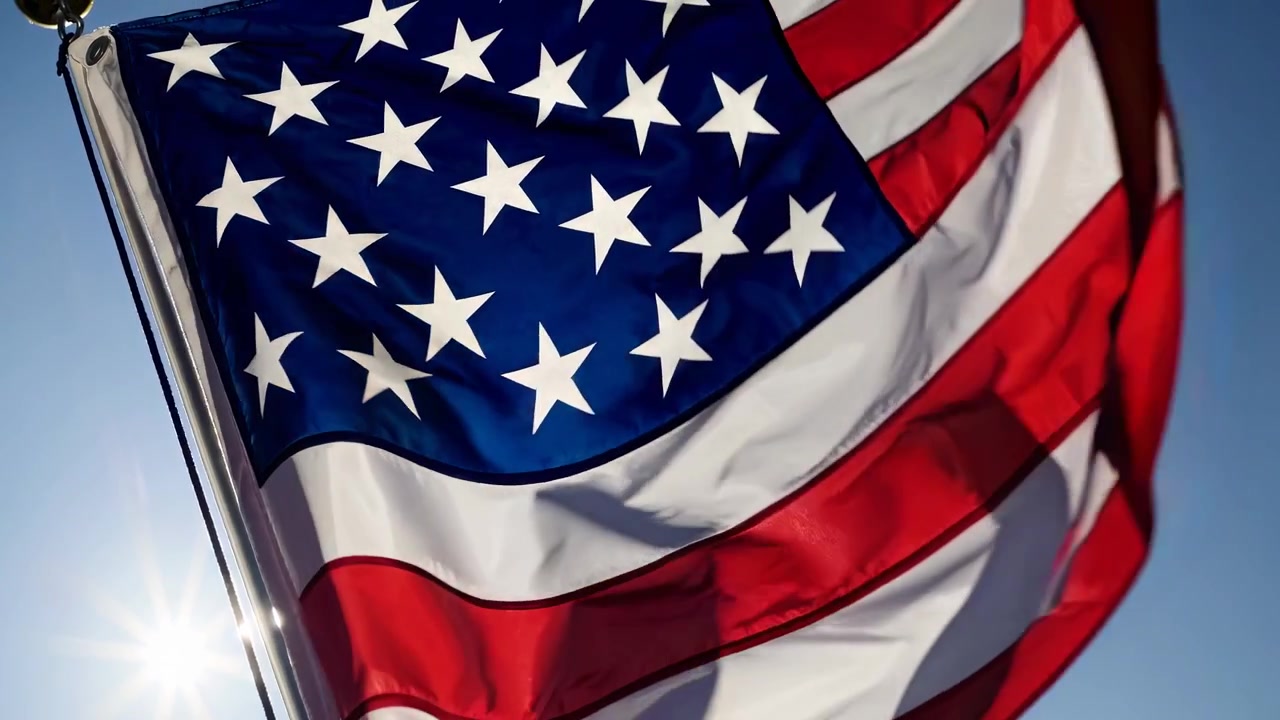 Bandiera americana che sventola al vento contro un cielo blu con bagliore solare.