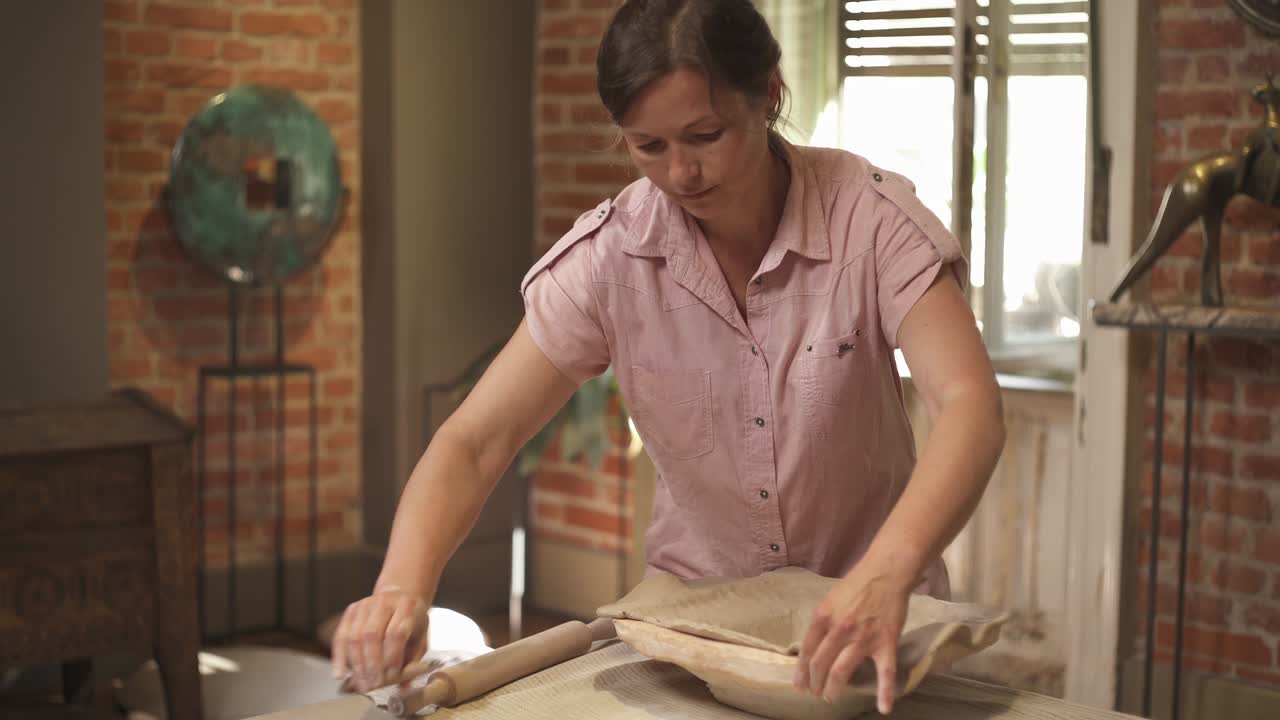 A close-up of an inspired young female potter shaping clay plate. Ceramics made with professional tools. Artist working in workshop. Creating modern art product