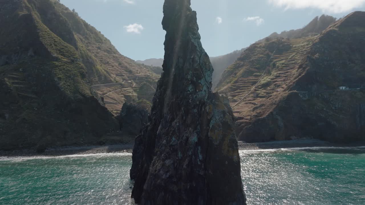 Dynamic aerial orbit of Ilhéus da Ribeira da Janela’s iconic rock formation, revealing the natural arch against Madeira’s mountainous coastline.