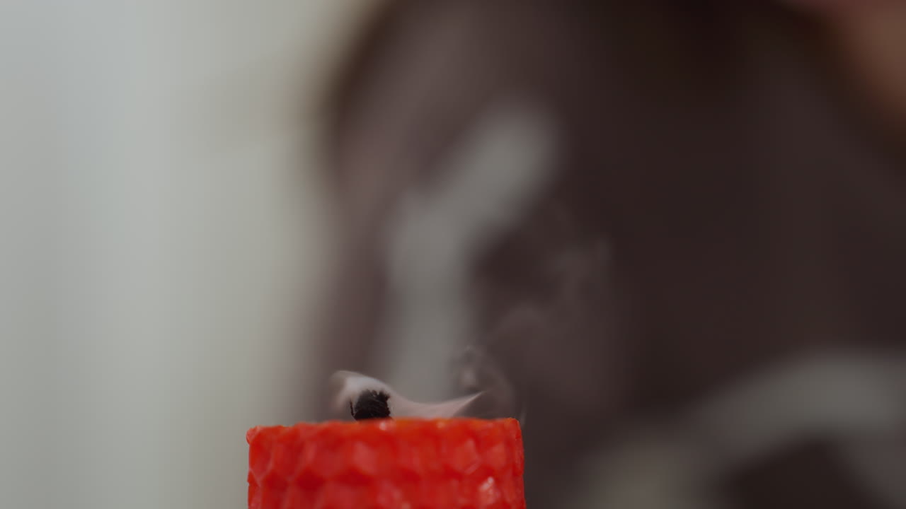 экстремальный крупный план пламени красной свечи, с размытой фигурой на заднем плане, кусочки дыма поднимаются по мере того, как пламя исчезает, создавая успокаивающую и отражающую атмосферу