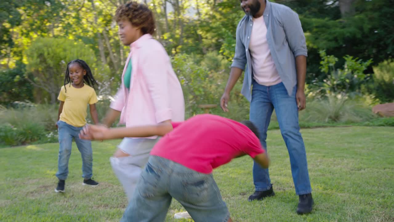 Familia afroamericana jugando fútbol casualmente en el patio trasero, la niña regateando el balón, el niño desafiando.