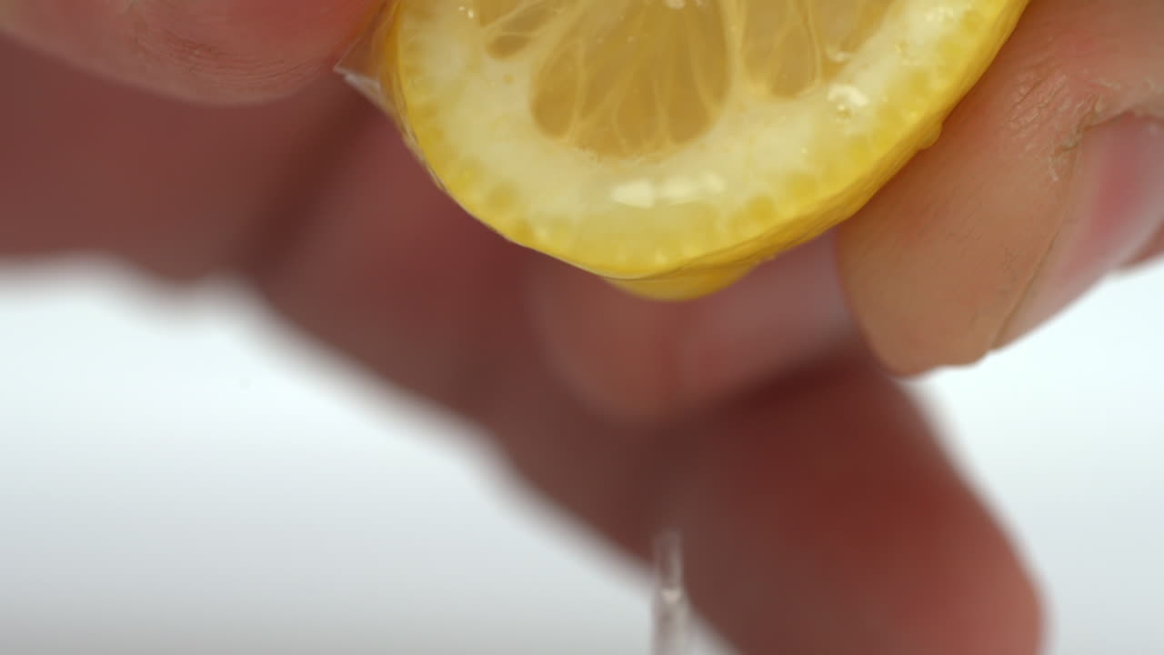 Vídeo macro a cámara lenta de una mano exprimiendo la jugosa pulpa de medio limón mientras fluye zumo recién exprimido y cae una sola pepita, capturado con todo detalle.