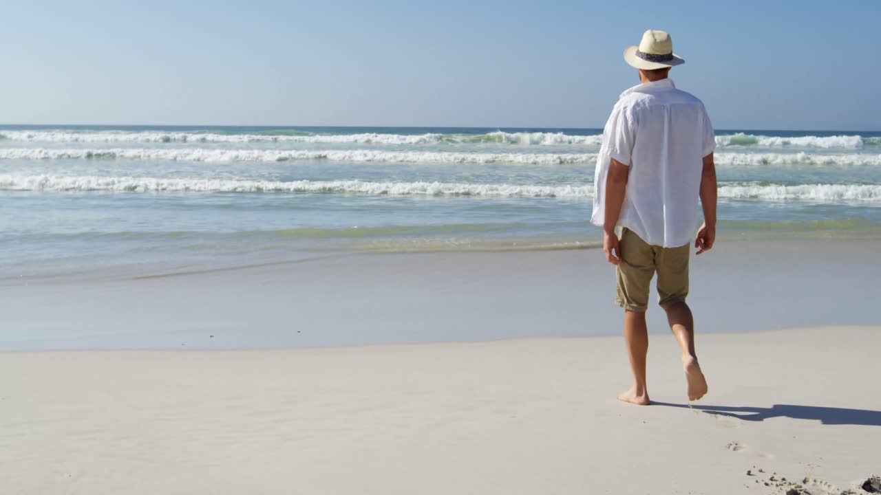 hombre con sombrero caminando por la playa en un día soleado 4k