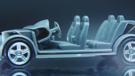 a tiny model metal sample skeleton of a car on a rotating stand with studio lights, macro close up shot, 4k video, silver wheels, black tires, doors and windows