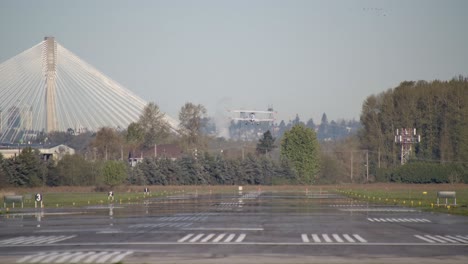 Biplane-Takes-Off-From-the-Runway,-Port-Mann-Bridge-in-Surrey-Backdrop