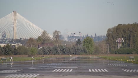 el biplano despega de la pista, el puente de port mann en el fondo de surrey