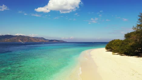 beautiful white beach bordered by lush vegetation and blue turquoise lagoon on a bright blue sky with white clouds background in indonesia