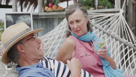 una pareja caucásica feliz bebiendo y hablando en una hamaca fuera del bar de la playa, en cámara lenta.