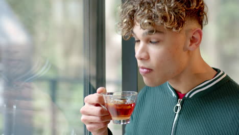 young man enjoying hot tea by window, reflecting and relaxing indoors