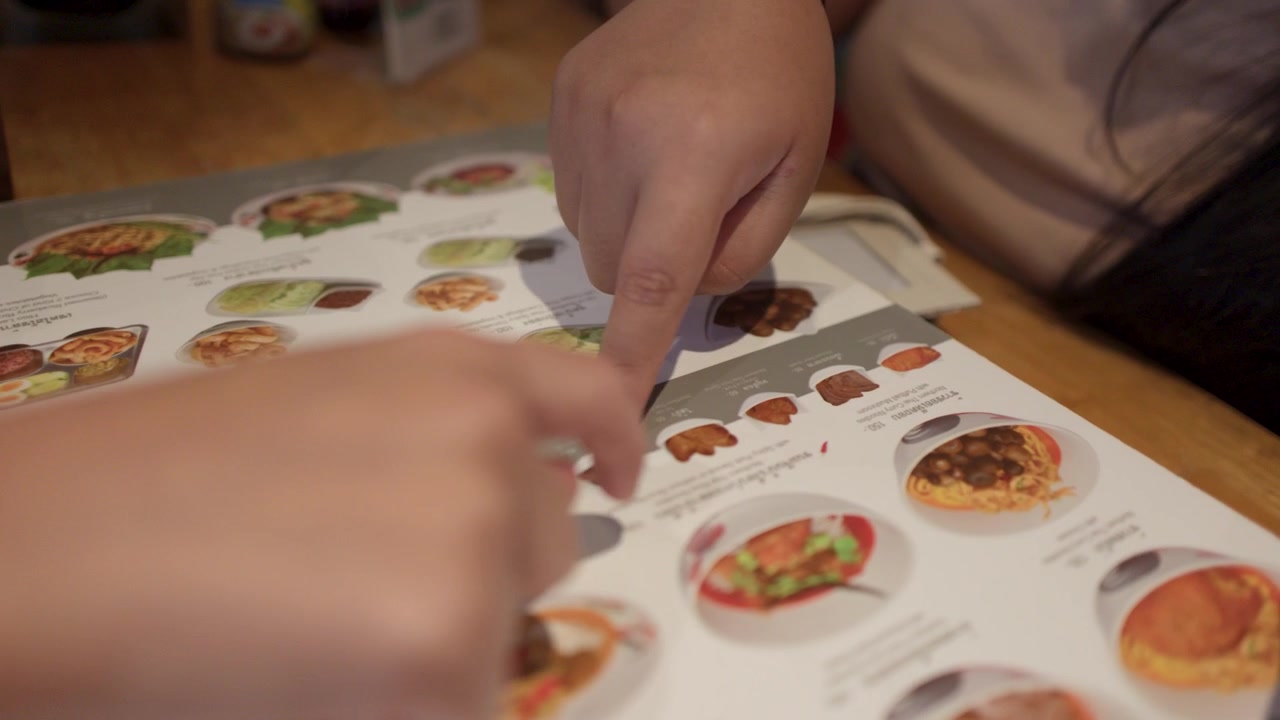 To personer peger på madvarer på en papirmenu, mens de spiser i Bangkok.