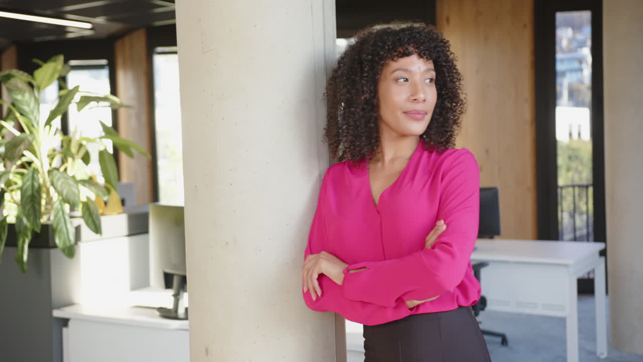 Confident businesswoman in pink blouse standing with arms crossed in office
