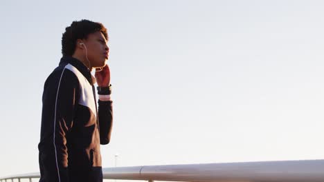 African-american-man-putting-earphones-on-during-exercise-outdoors-by-seaside