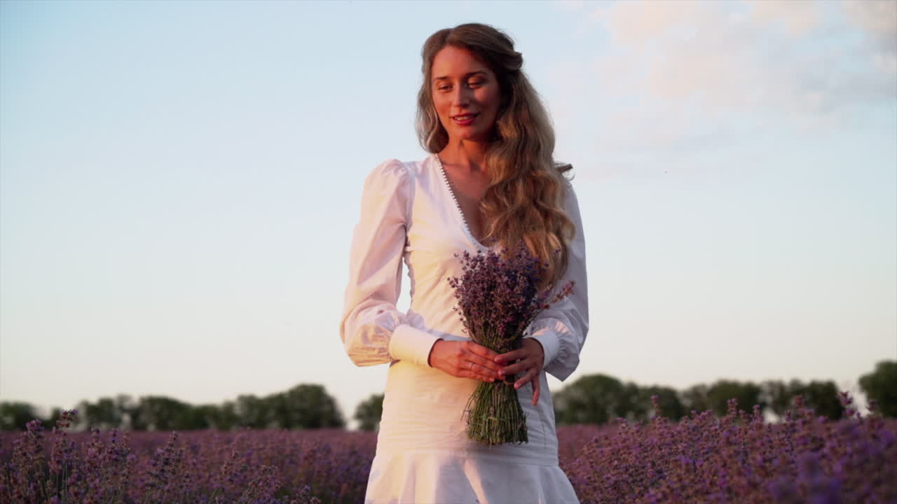 Donna con un abito bianco che tiene in mano un bouquet di lavanda in un campo
