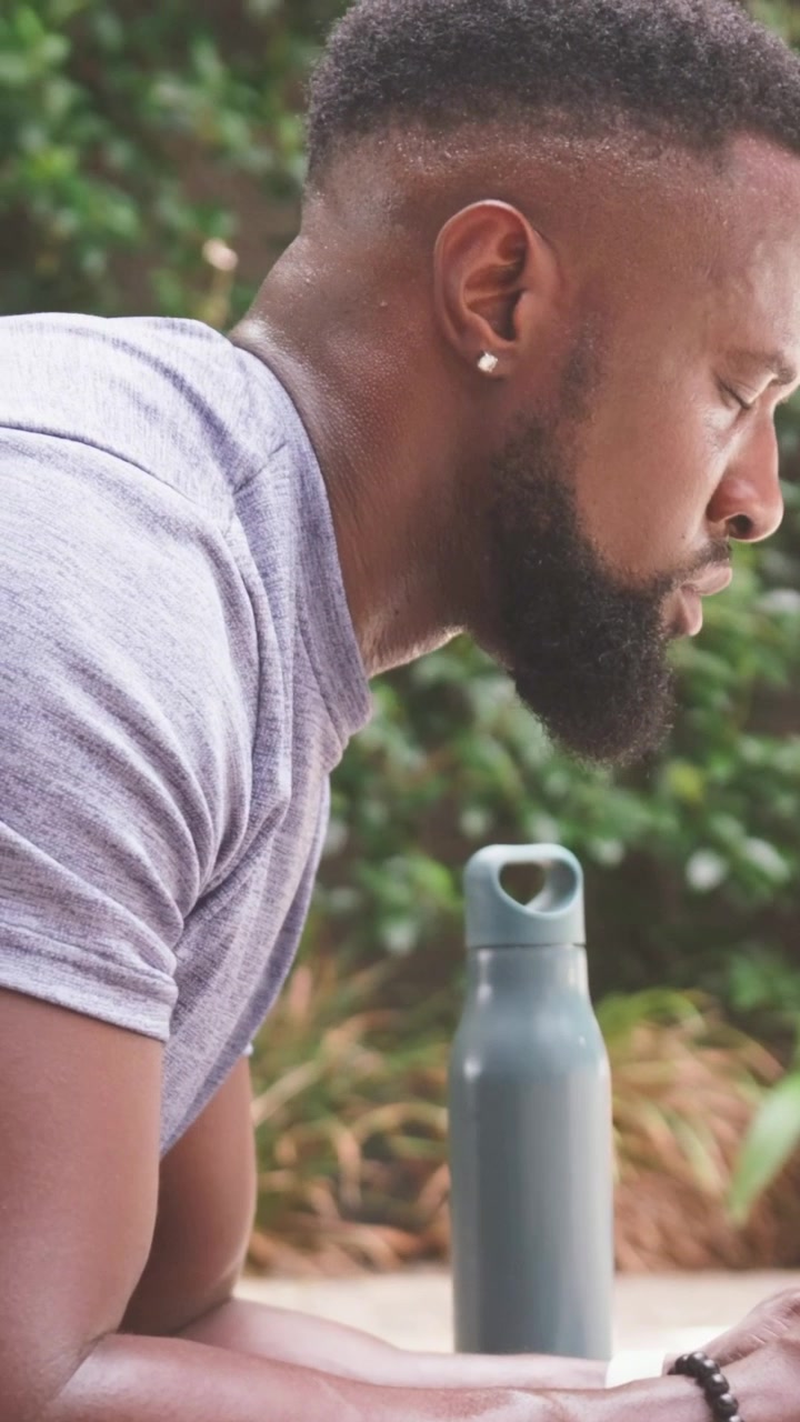 Vertical video: Noticing offscreen device, man in gray tee leaning on patio with water bottle