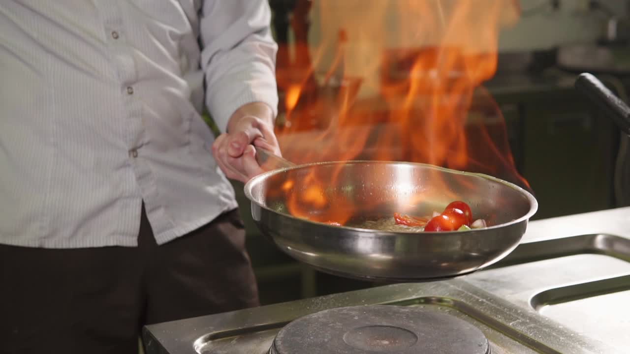 chef cocinando verduras en una sartén con llamas