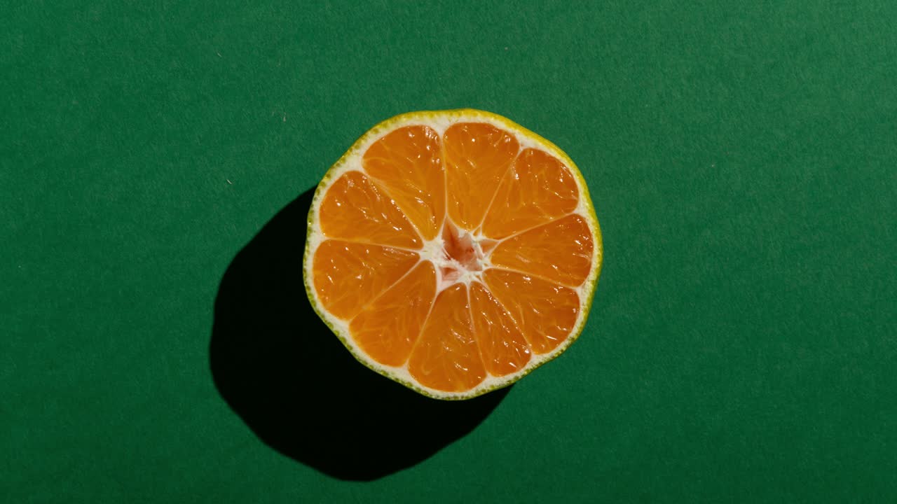 Mezze mandarini freschi con ombra marcata su sfondo verde. Animazione in stop motion