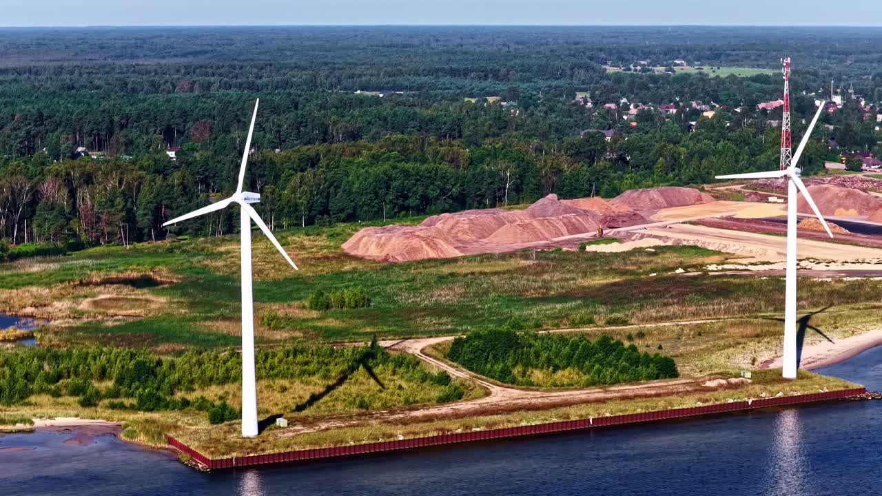 Green energy wind turbines at coastal industrial site from drone view