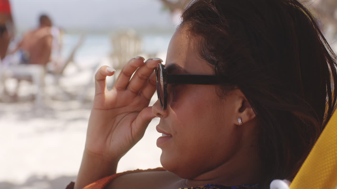 Ragazza latina in posa per un primo piano sorridente, togliendosi gli occhiali da sole, mentre si rilassa in un resort sulla spiaggia caraibica.