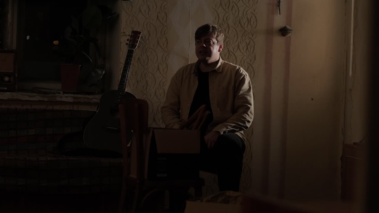 Pretty young man sitting near guitar while sitting on sofa in dark living room