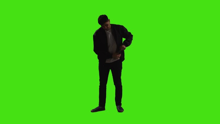 Giovane uomo che risponde al cellulare in piedi davanti a schermo verde con illuminazione a bassa chiave.