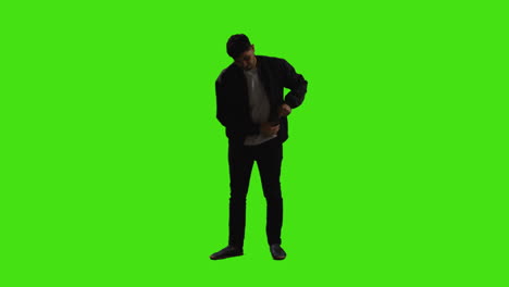 Young-Man-Answering-Call-On-Mobile-Phone-Standing-Against-Green-Screen-With-Low-Key-Lighting