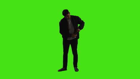 joven respondiendo a una llamada en un teléfono móvil de pie contra la pantalla verde con una iluminación de baja clave