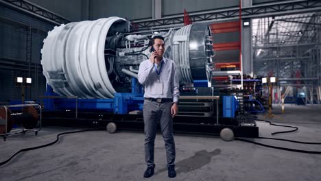 full body of an asian male professional worker standing with airplane engine maintenance conducted, analytics checking the turbine, he is speaking with someone in the phone