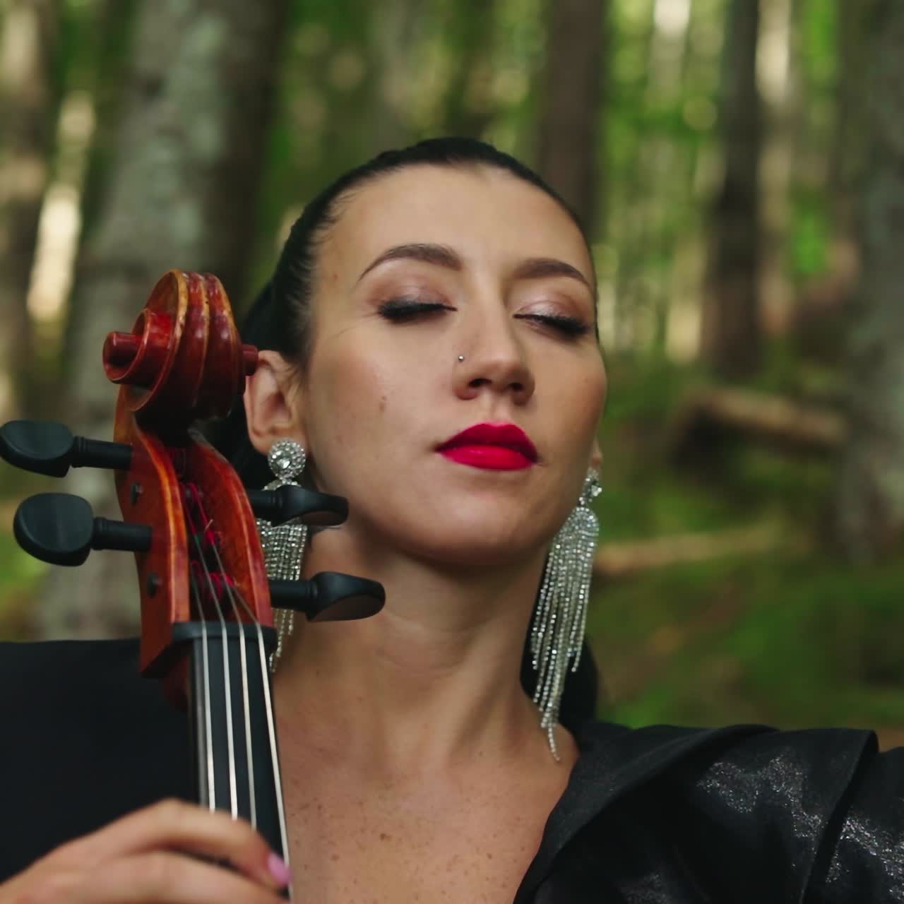 Woman with cello in the forest. Portrait of a dark-haired woman playing the musical instrument on green nature background. Close-up.