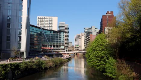 sunny day view of manchester cityscape with modern buildings alongside a calm river