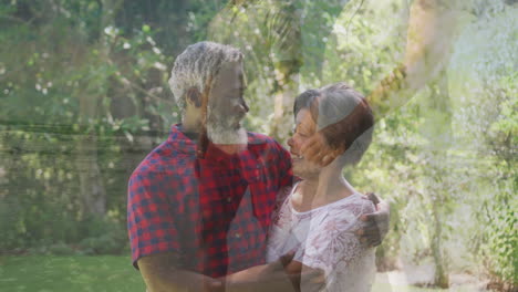 in garden, elderly couple embracing surrounded by trees and greenery in sunlight